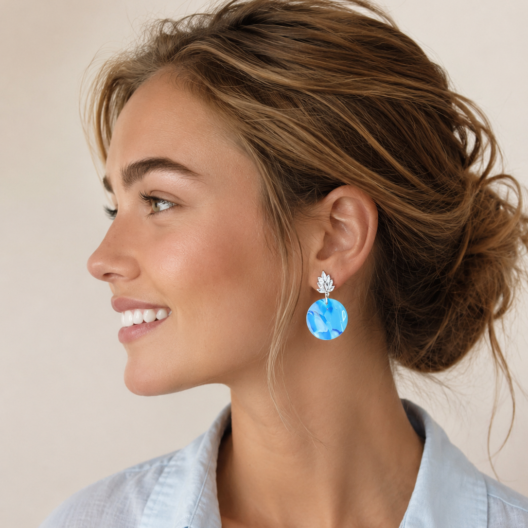 A woman in profile wearing a light blue button-down shirt and a dangling earring with a faceted light blue gemstone and a silver-toned setting.