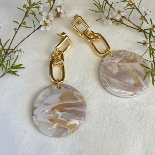 Gold chain earrings with marbled circular pendants on a white background with floral elements.
