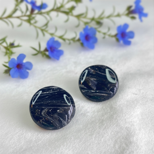 Black marbled circular objects on a white surface with blue flowers in the background