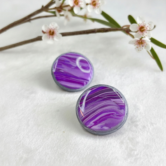 Purple and gray marbled round earrings on a white surface with a branch of flowers.