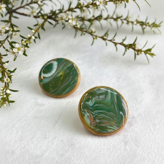Green marbled earrings on a white surface with green leaves in the background