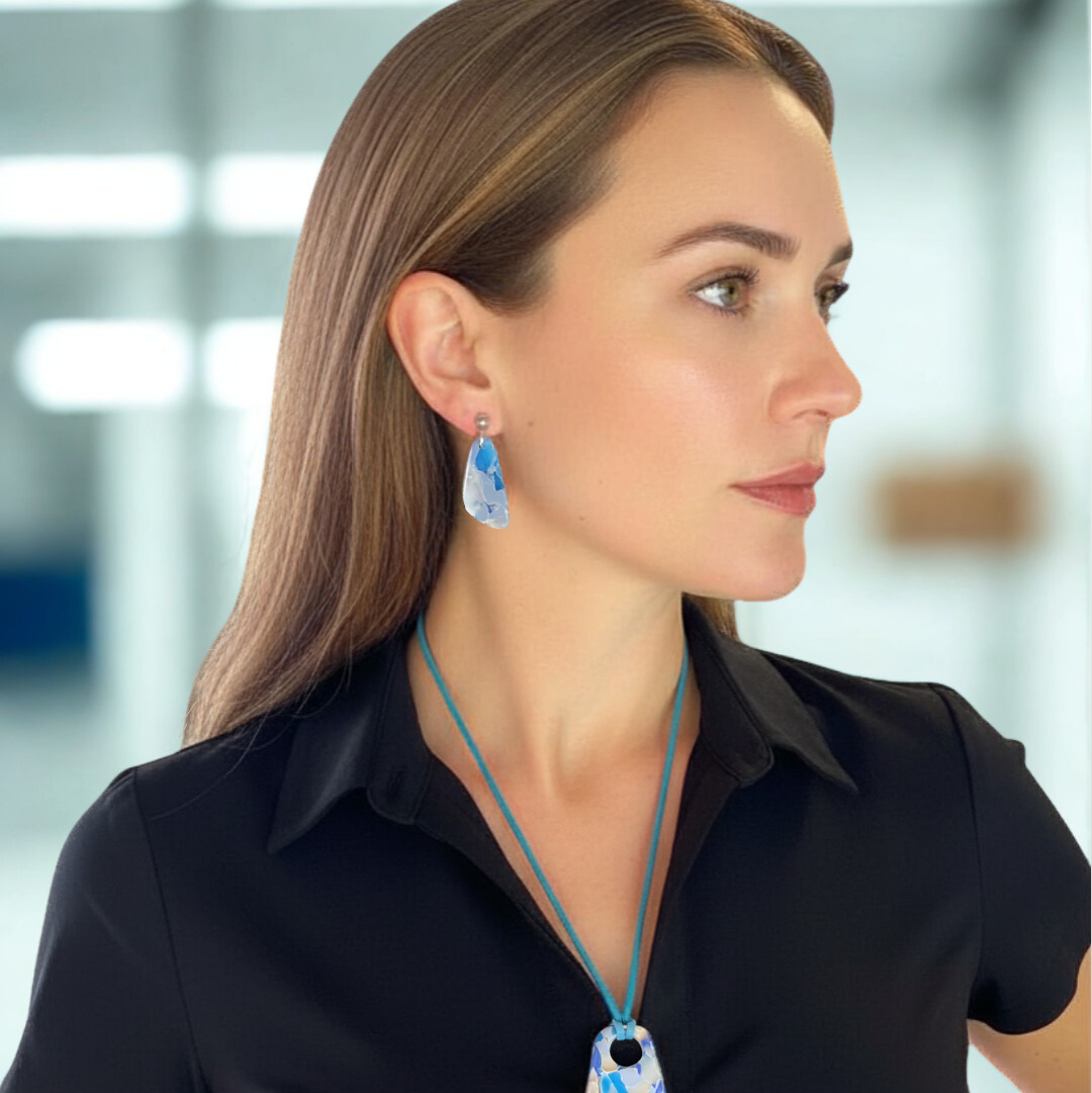 Woman wearing a black shirt with a blue pendant and earrings against a blurred indoor background